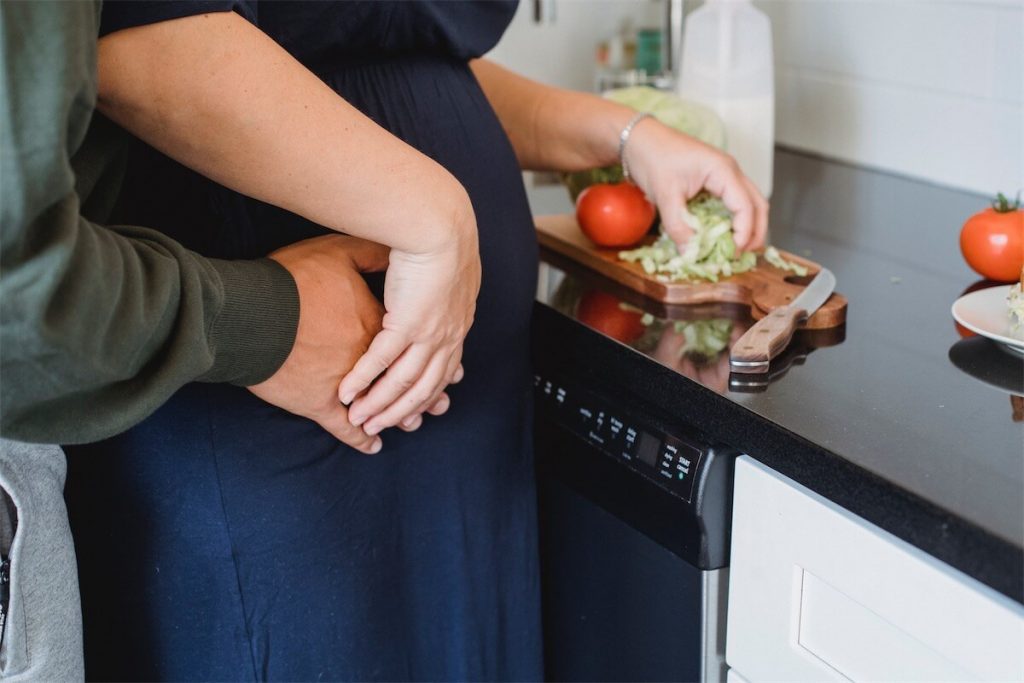 Pregnant wife and husband preparing salad in the kitchen, discussing their plans for upgrading their home through refinancing