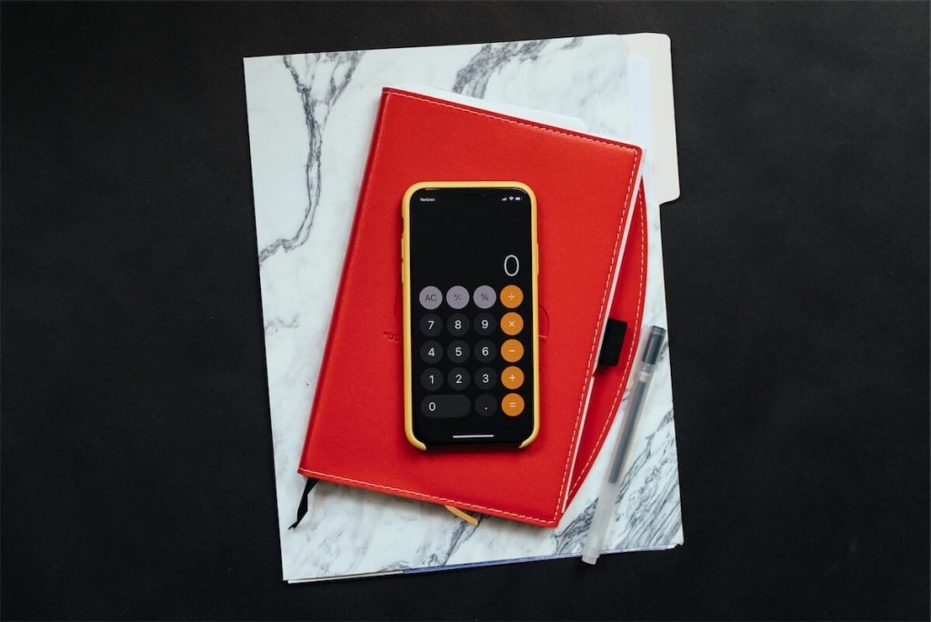 A phone calculator on top of a notebook and laptop. The calculation of your ABSD is dependent on your residency status and the number of properties you own